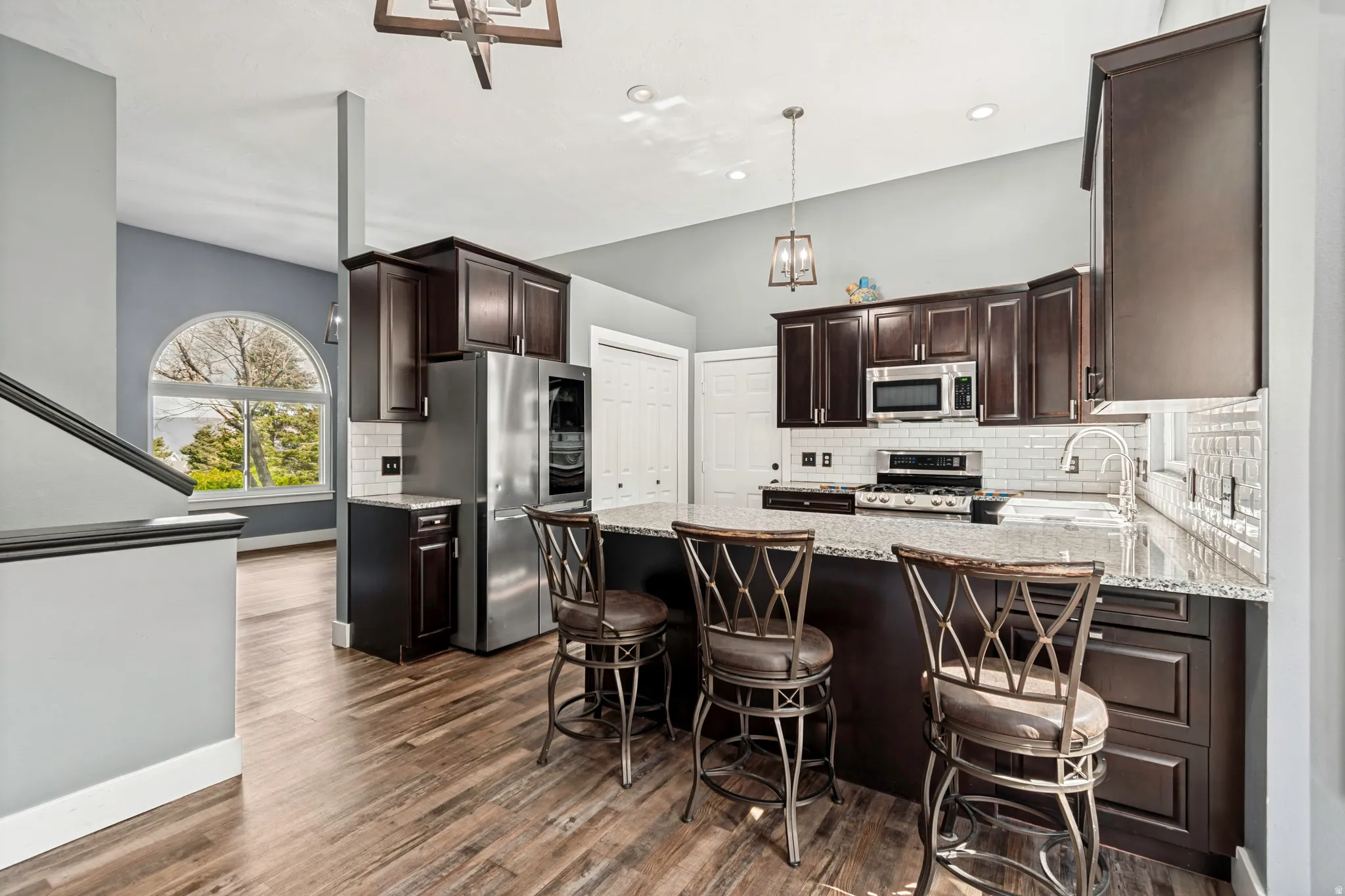 Spacious kitchen featuring dark wood cabinetry, stainless steel appliances, a white subway tile backsplash, and a large island with a stone countertop