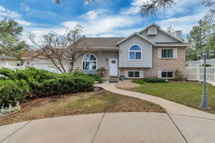 Split-level residence featuring a brick and siding exterior, arched window, two-car garage, and a white picket fence enclosing the side yard