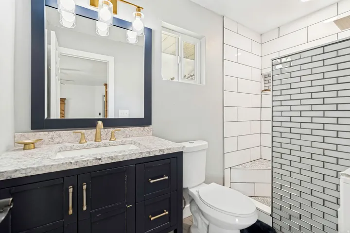 Bathroom featuring a dark wood-finish vanity with a light speckled countertop, an undermount sink, and brass-finish fixtures