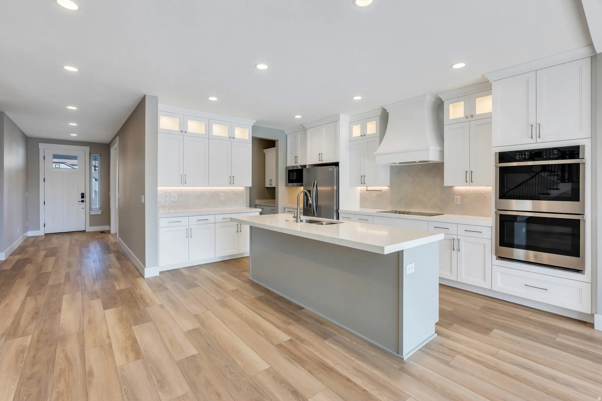 Open-concept kitchen featuring an expansive island with a light gray base, white countertop, and stainless steel sink