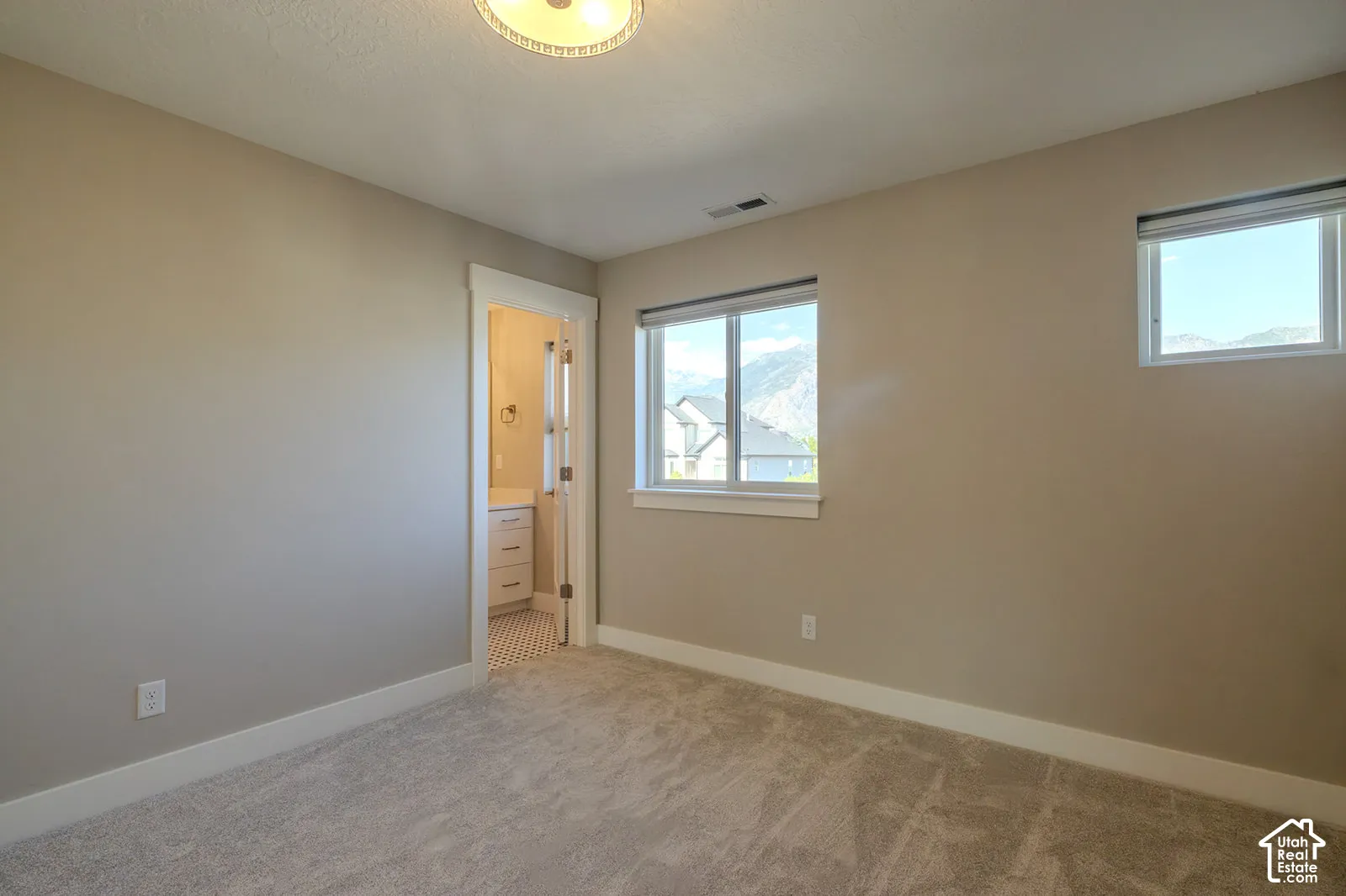 Carpeted room featuring two windows with mountain scenery, an overhead ceiling light, and an en-suite bathroom with a vanity and hexagonal floor tiling