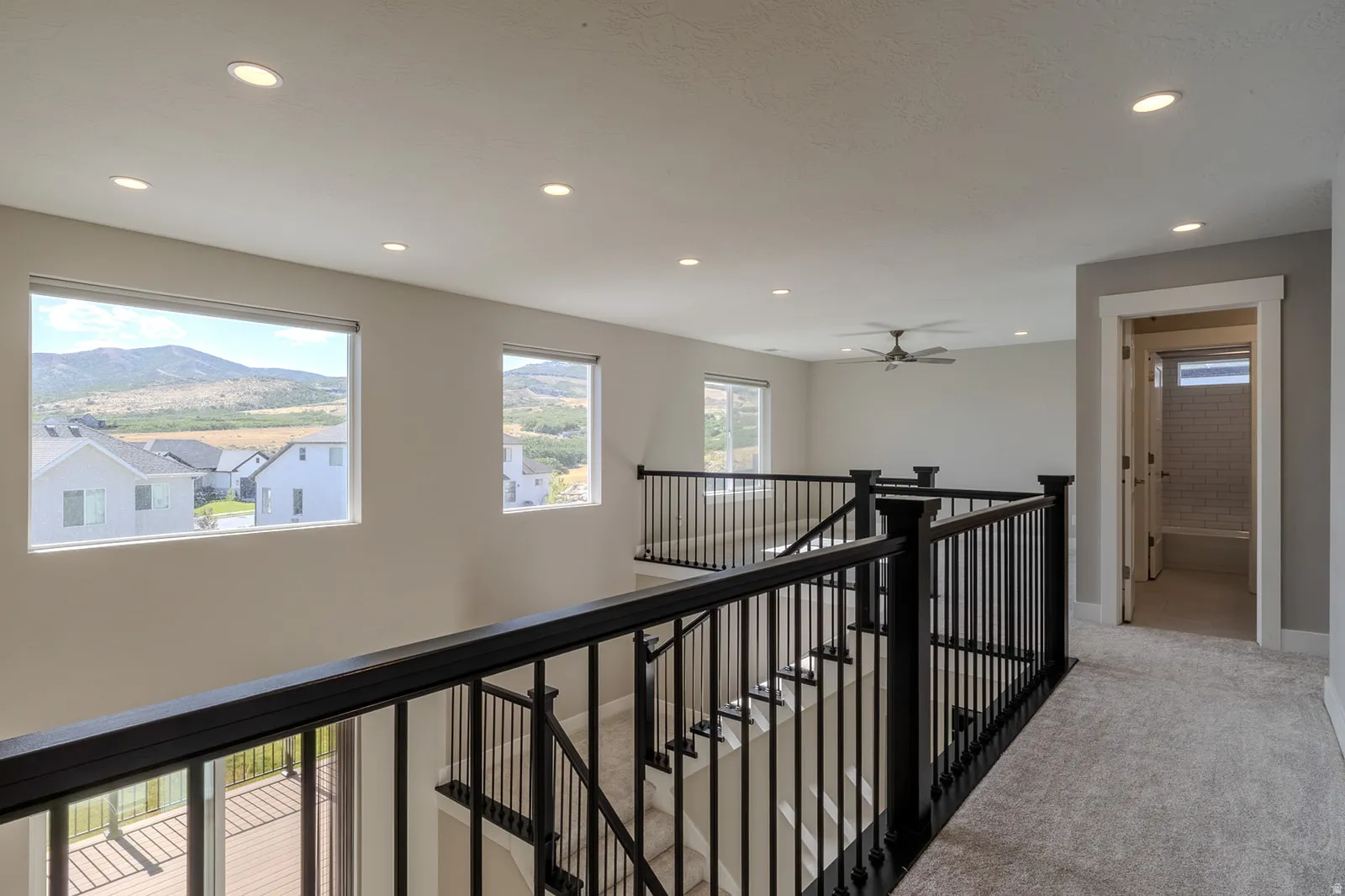 Upper-level landing featuring black wrought iron railing, recessed lighting, and wall-mounted ceiling fan