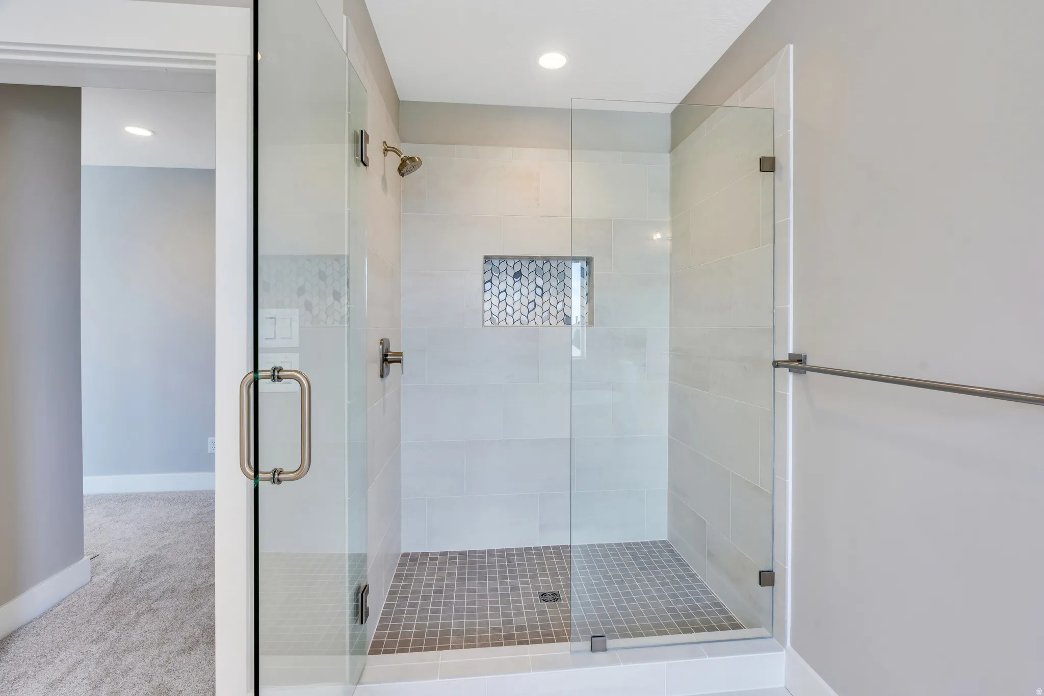 Primary bathroom with a glass-enclosed walk-in shower featuring large format wall tiles and a mosaic tile niche