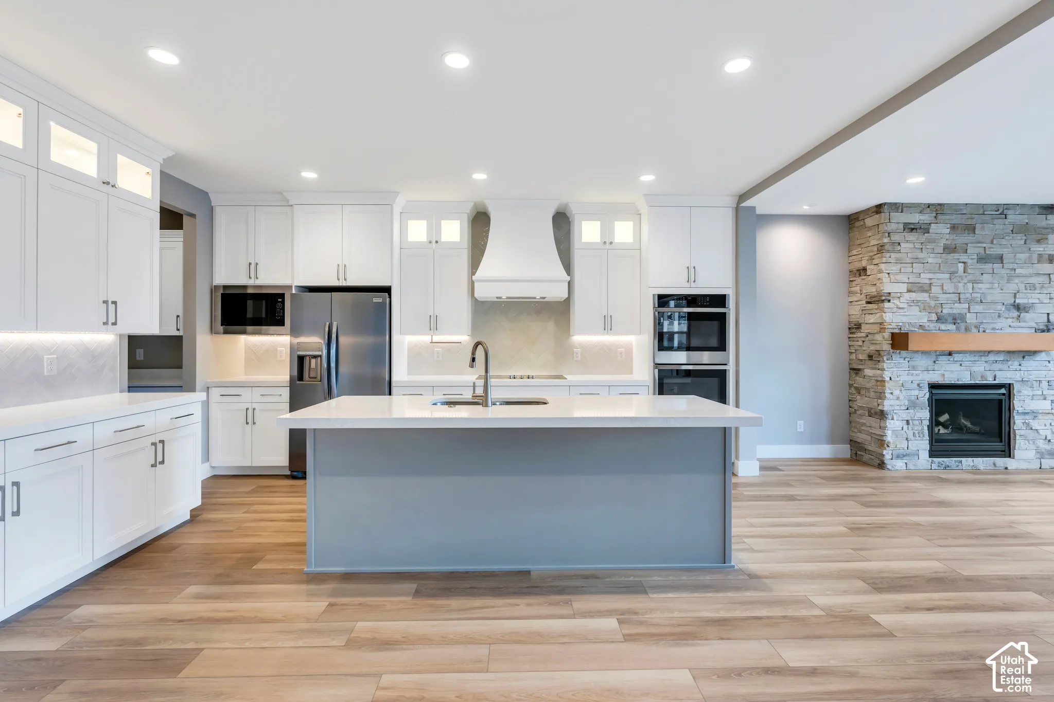 Open-concept kitchen featuring an island with a sink, white cabinetry with integrated lighting, stainless steel appliances, and wood-finish flooring