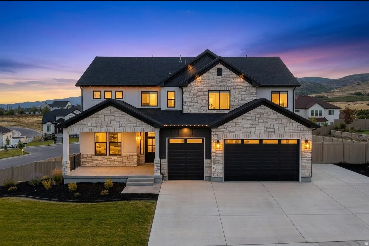 Contemporary two-story residence featuring a stone and stucco exterior, prominent black-framed windows, and a black shingled roof