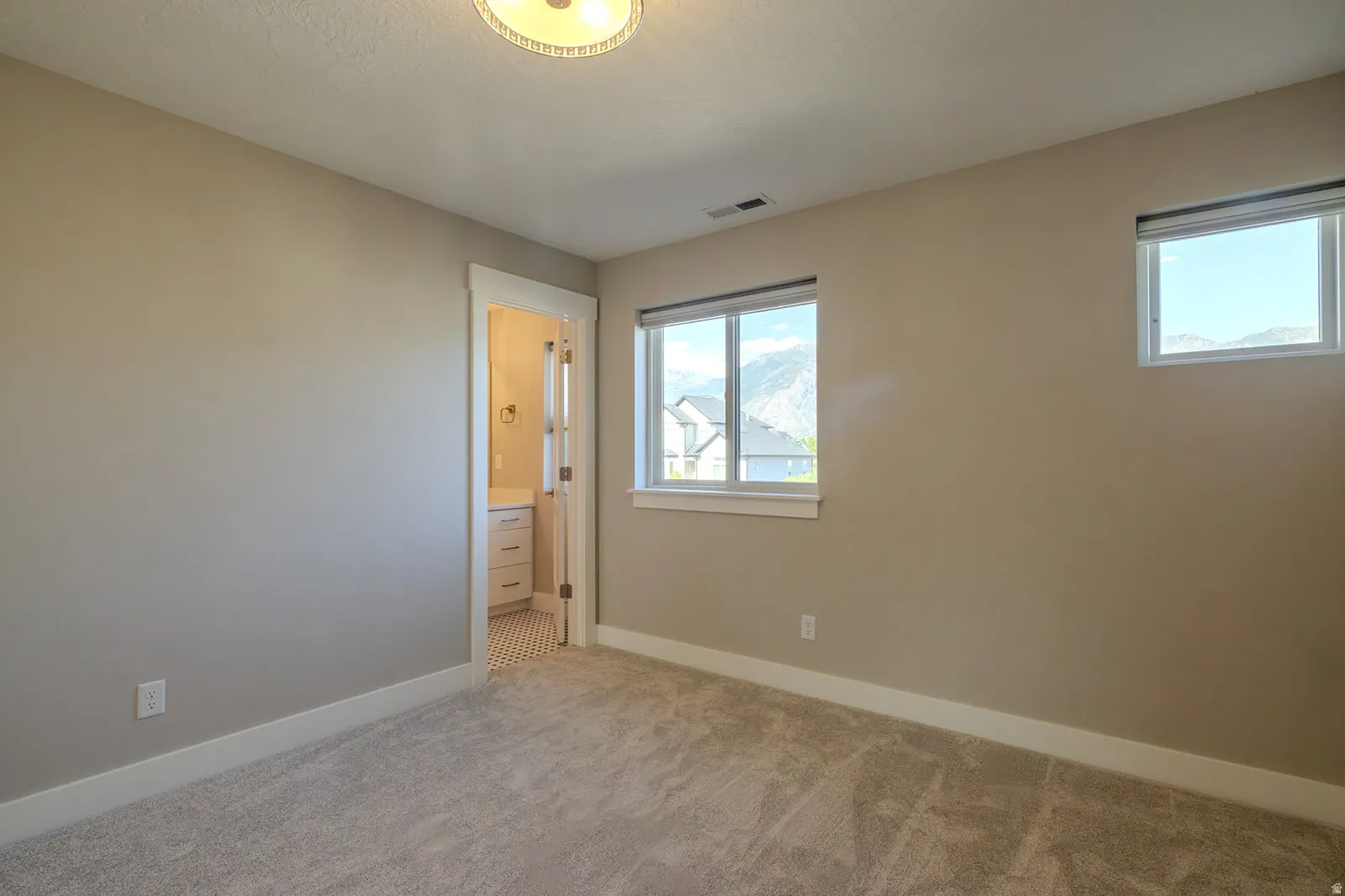 Carpeted room featuring two windows with mountain scenery, an overhead ceiling light, and an en-suite bathroom with a vanity and hexagonal floor tiling