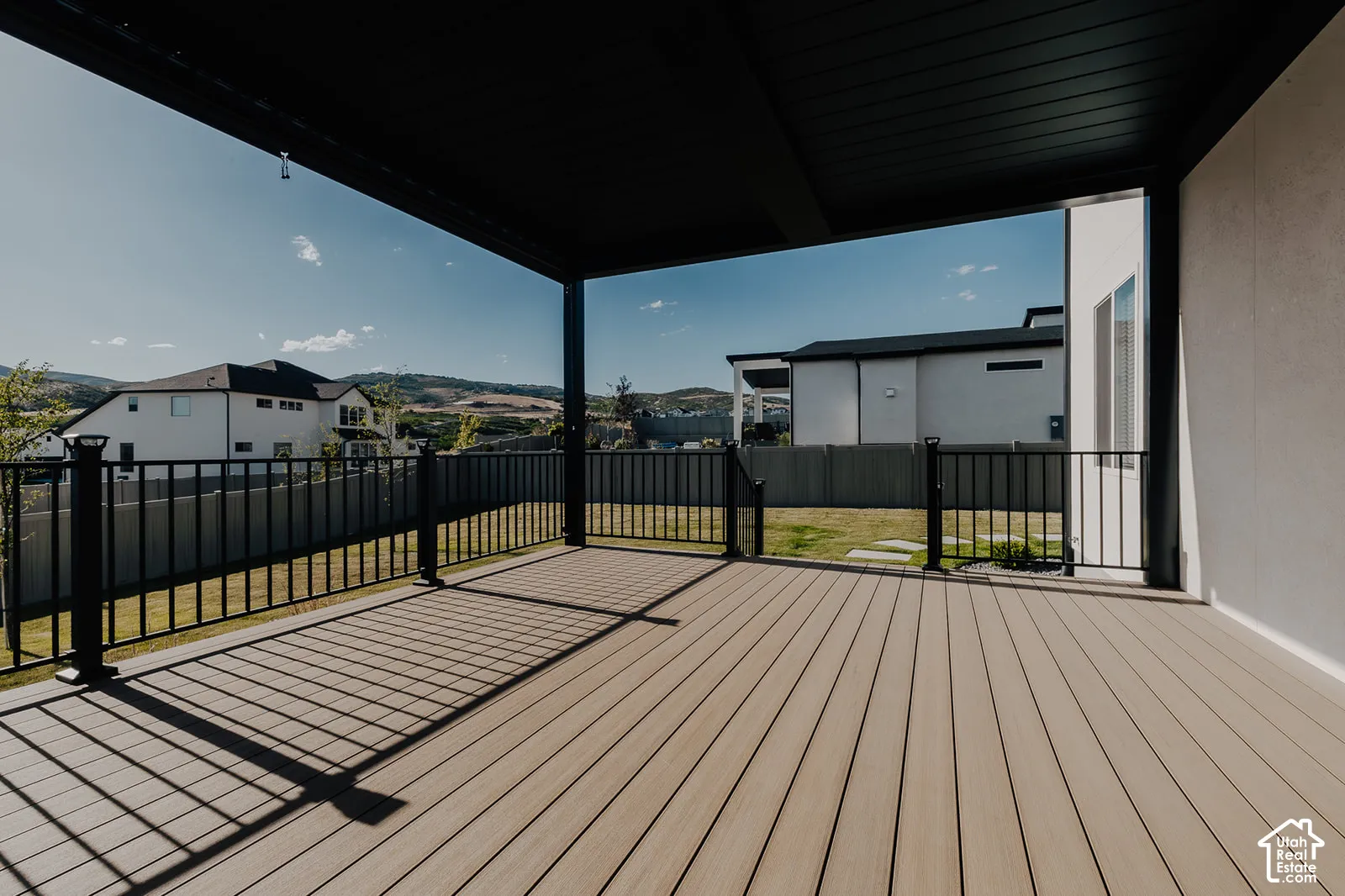 Covered outdoor deck with composite decking, black metal railings, and a stucco exterior wall