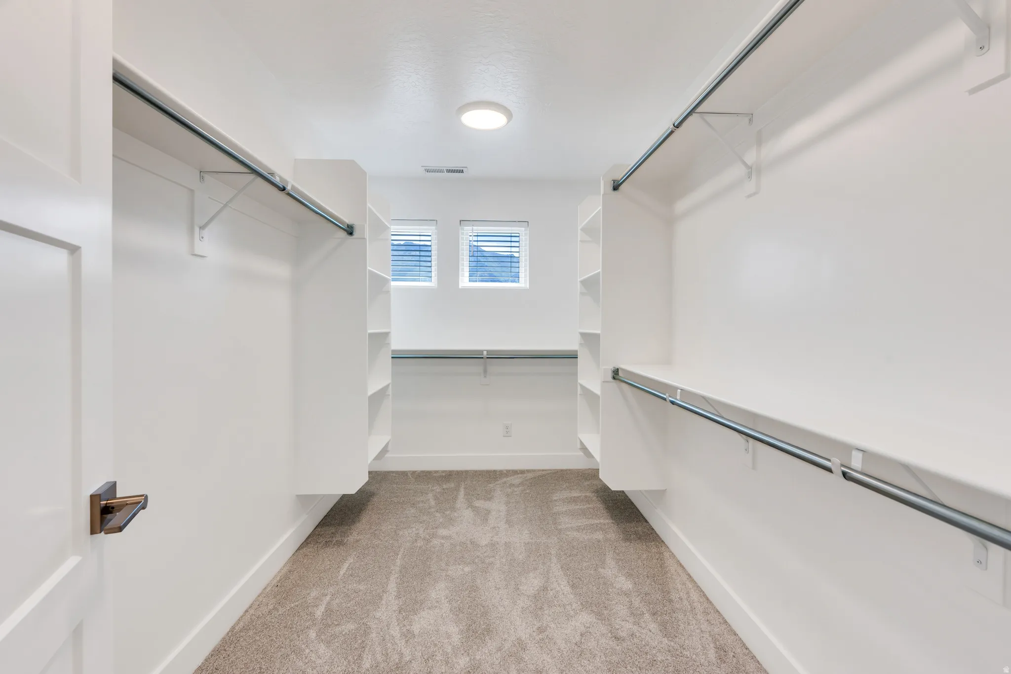 Primary room with a Spacious walk-in closet featuring built-in shelving, multiple hanging rods, recessed ceiling lighting, and two windows with blinds