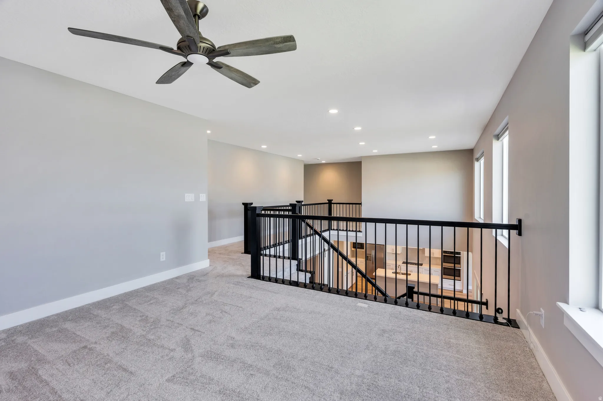 Carpeted open loft area featuring a ceiling fan, recessed lighting, and multiple windows