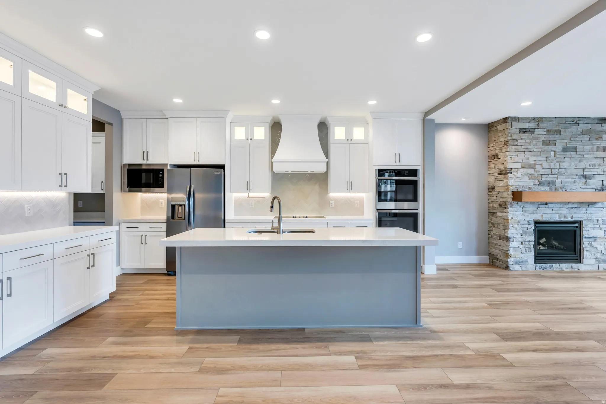 Open-concept kitchen featuring an island with a sink, white cabinetry with integrated lighting, stainless steel appliances, and wood-finish flooring