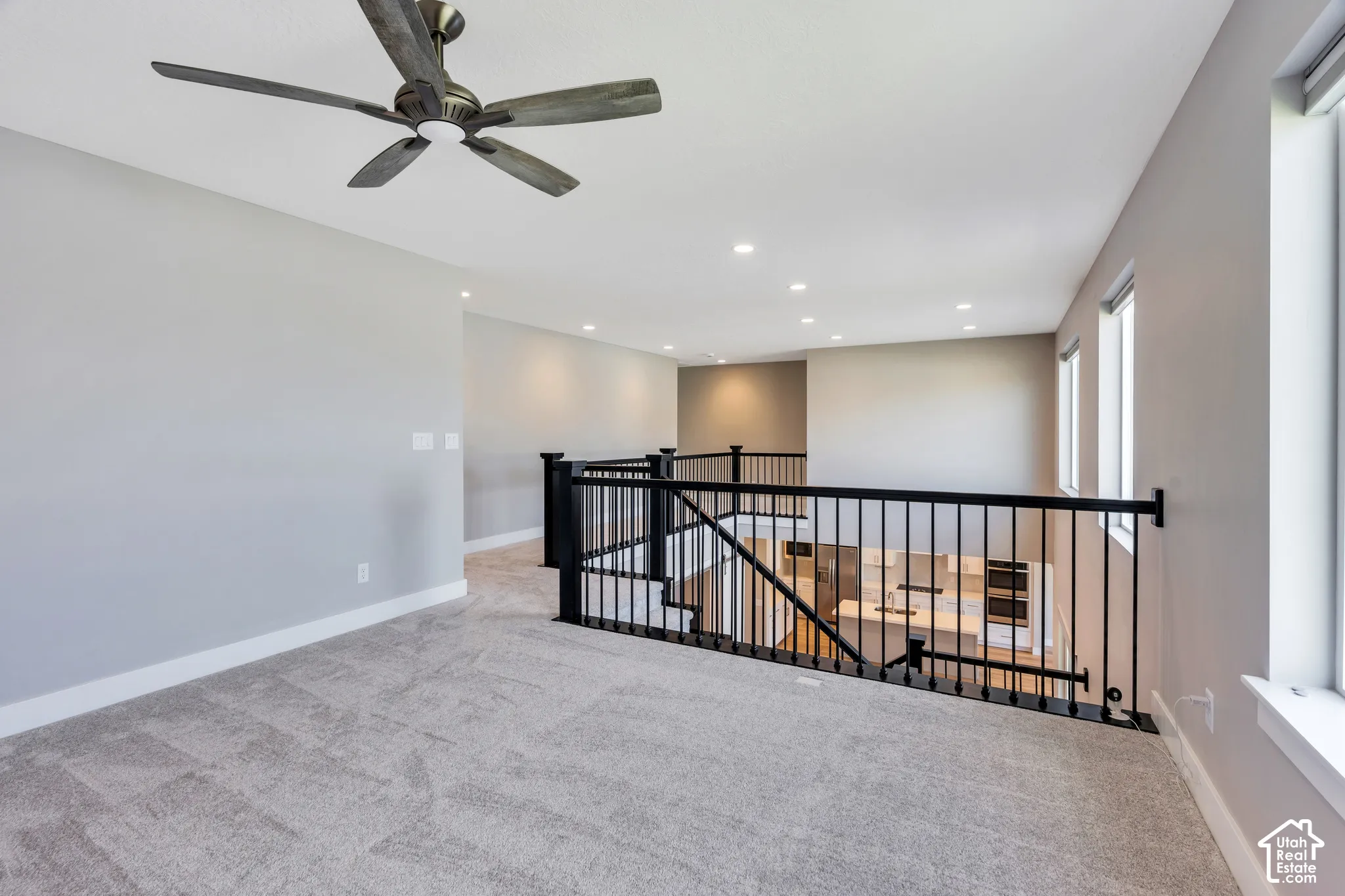 Carpeted open loft area featuring a ceiling fan, recessed lighting, and multiple windows