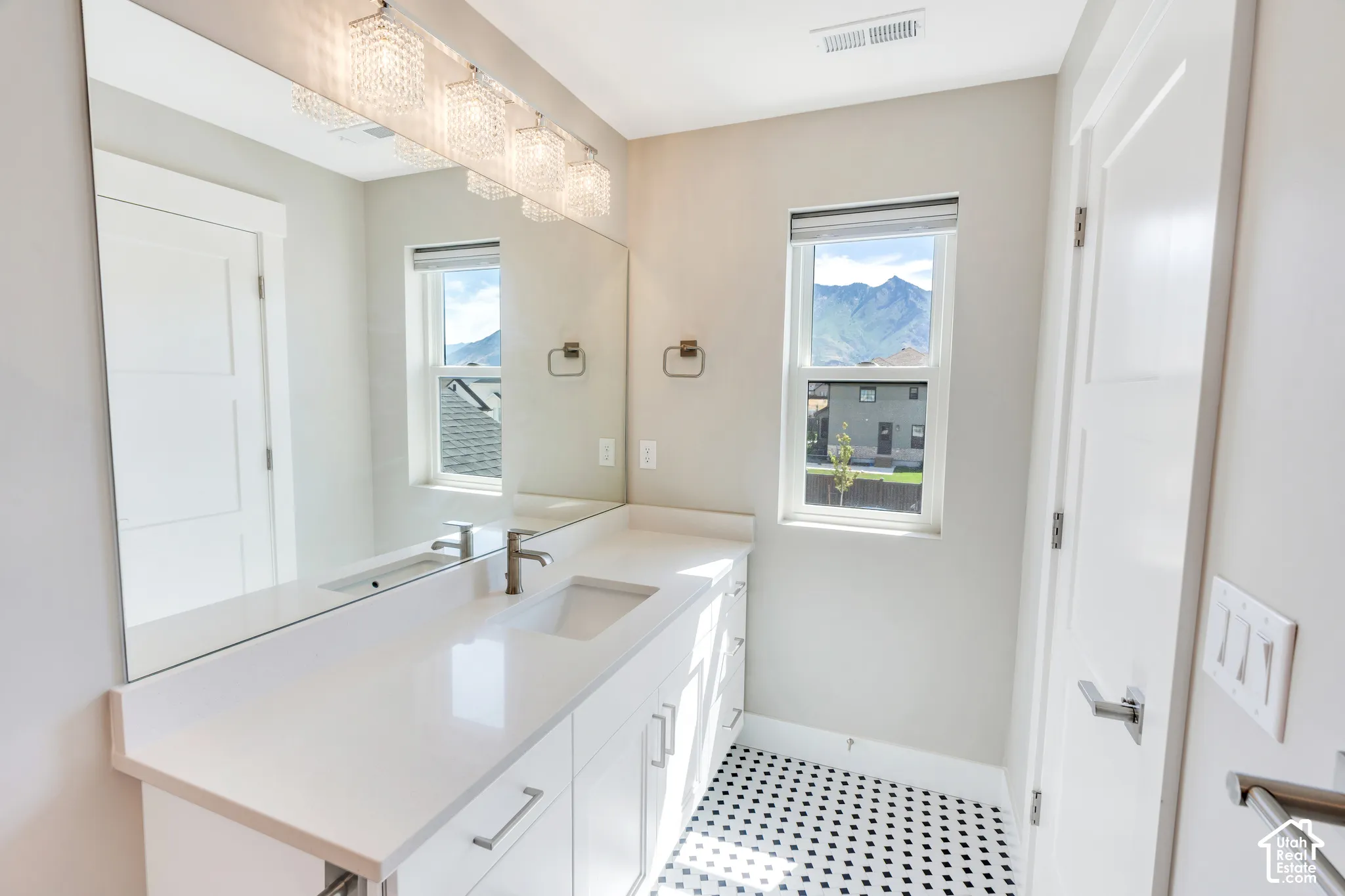 Bathroom featuring a full-width mirror, white vanity with integrated sink, and black and white penny tile flooring