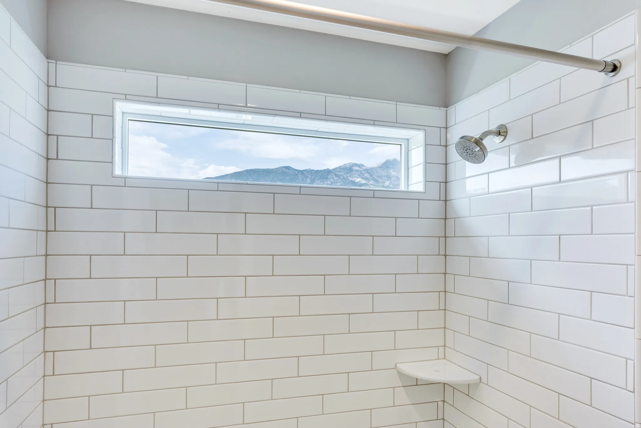 Shower with subway tile surround, featuring a transom window, built-in corner shelf, and brushed nickel shower head