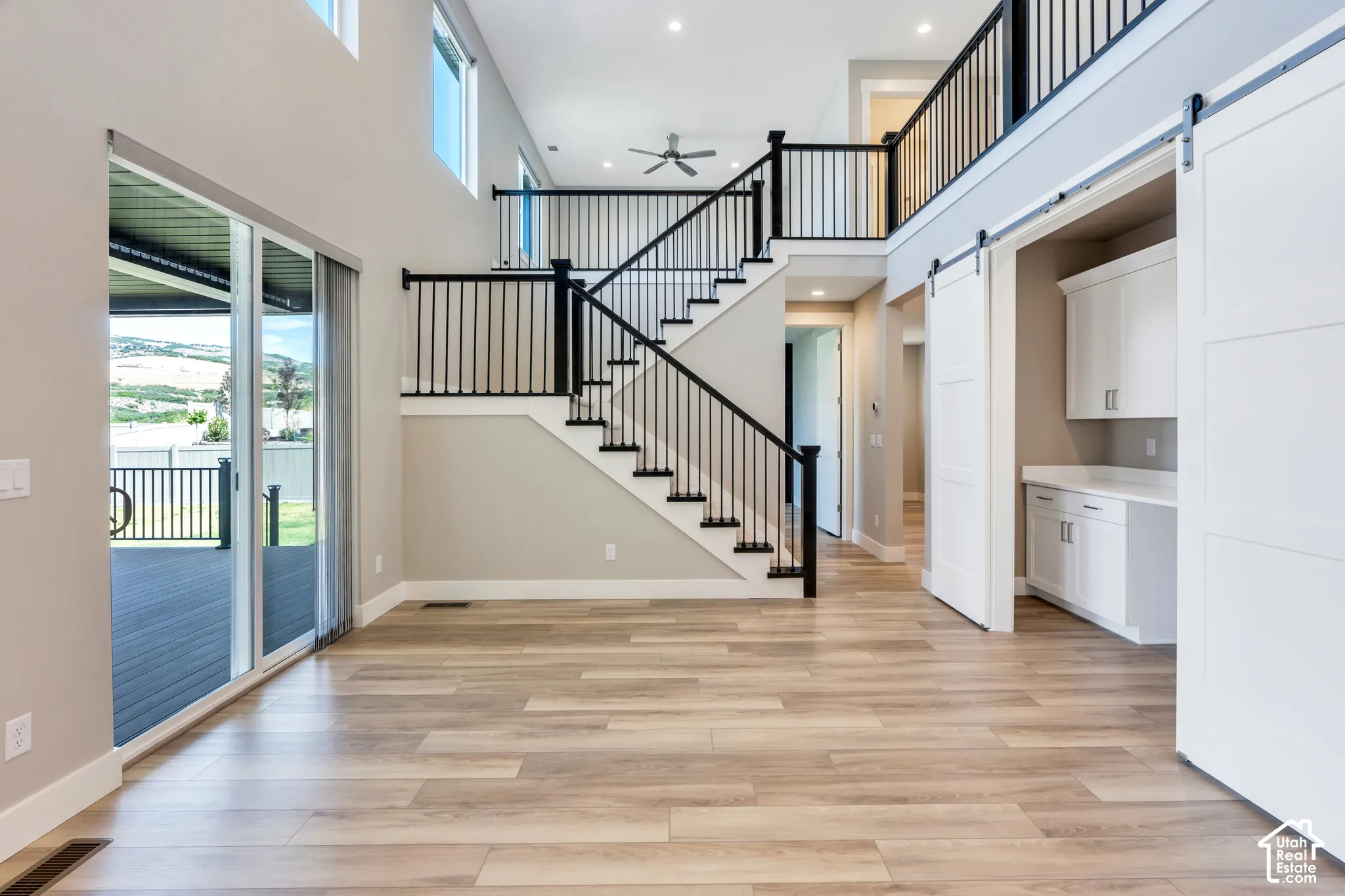 Two-story foyer featuring wood-finish flooring, a contemporary staircase with black railings, and a built-in desk area with white cabinetry and barn doors