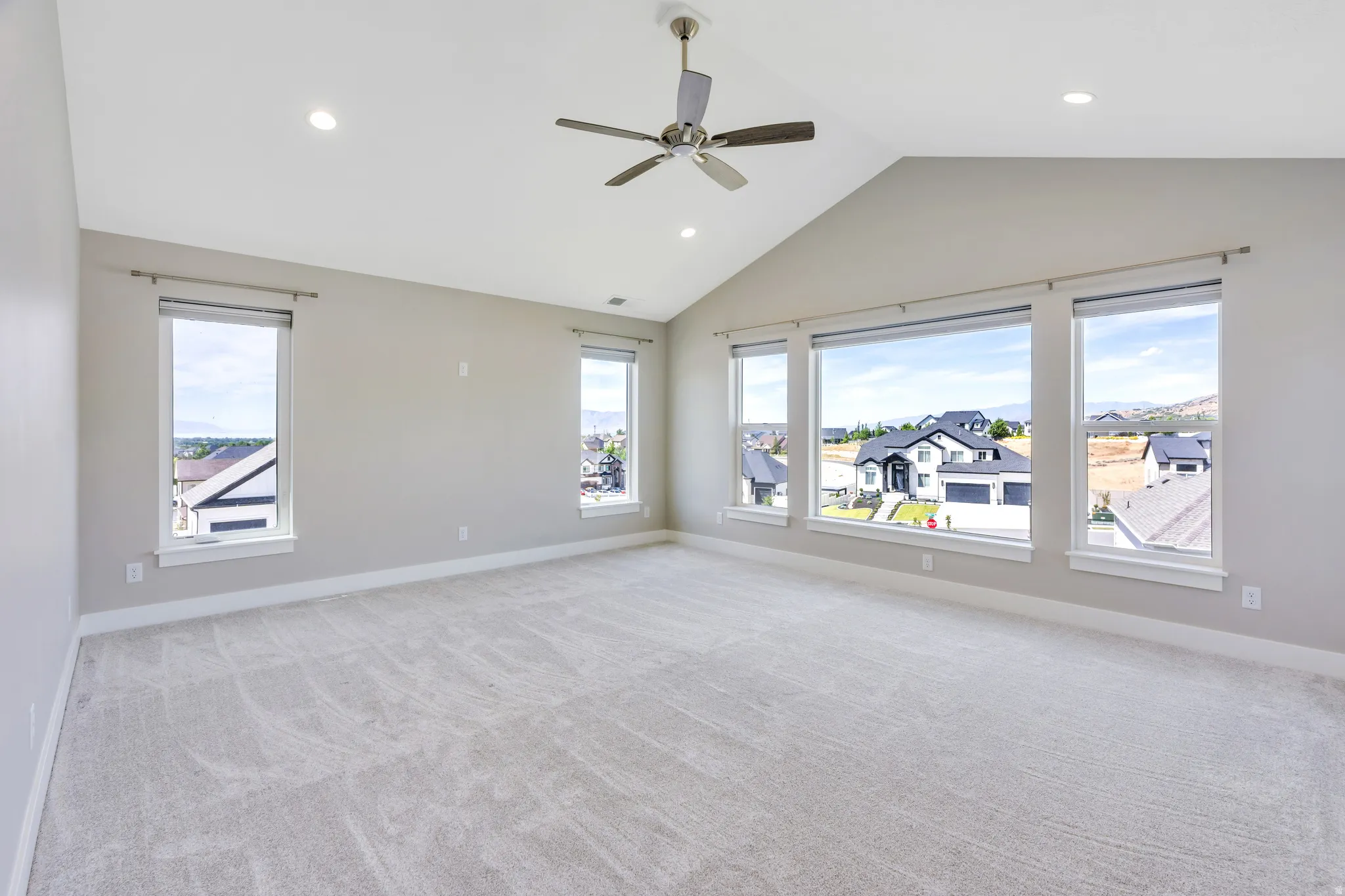 Spacious primary room featuring vaulted ceilings, recessed lighting, a ceiling fan, light-toned carpeting, and multiple windows providing ample natural light