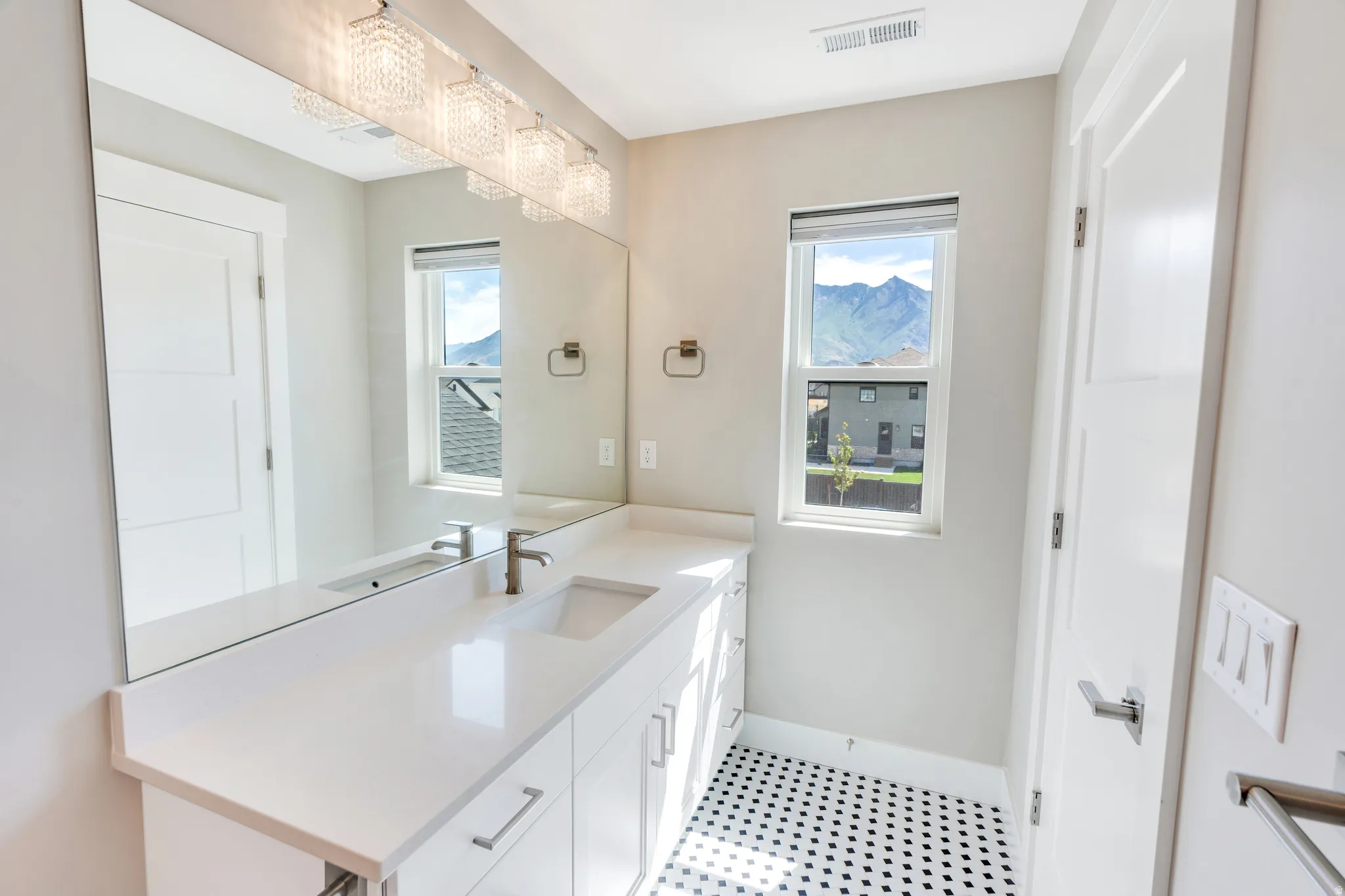 Bathroom featuring a full-width mirror, white vanity with integrated sink, and black and white penny tile flooring