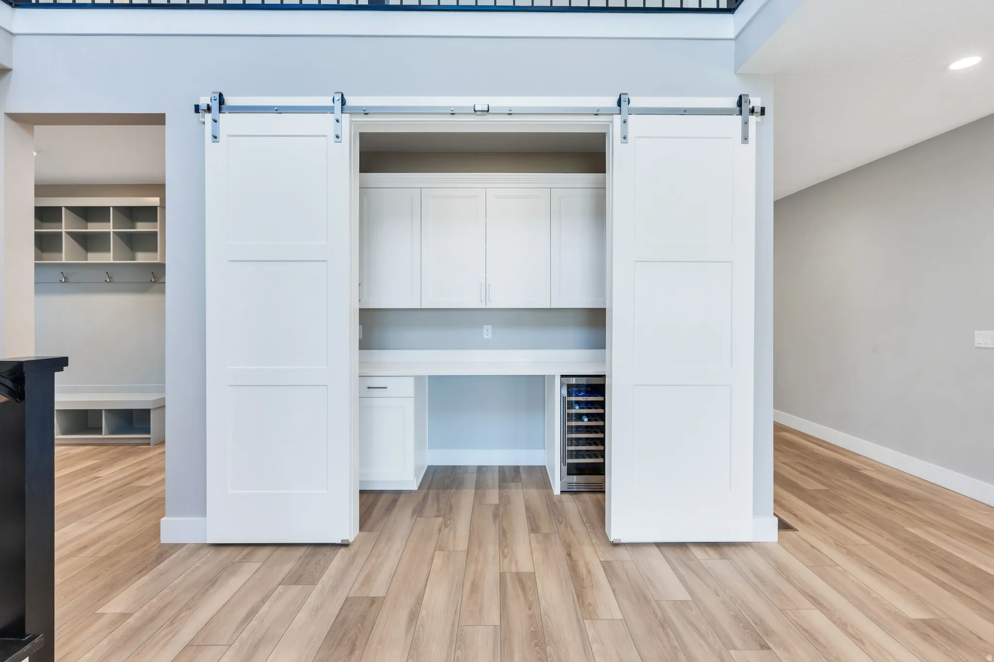 Built-in desk area featuring white cabinetry, a beverage refrigerator, and two white barn doors on a silver-tone track