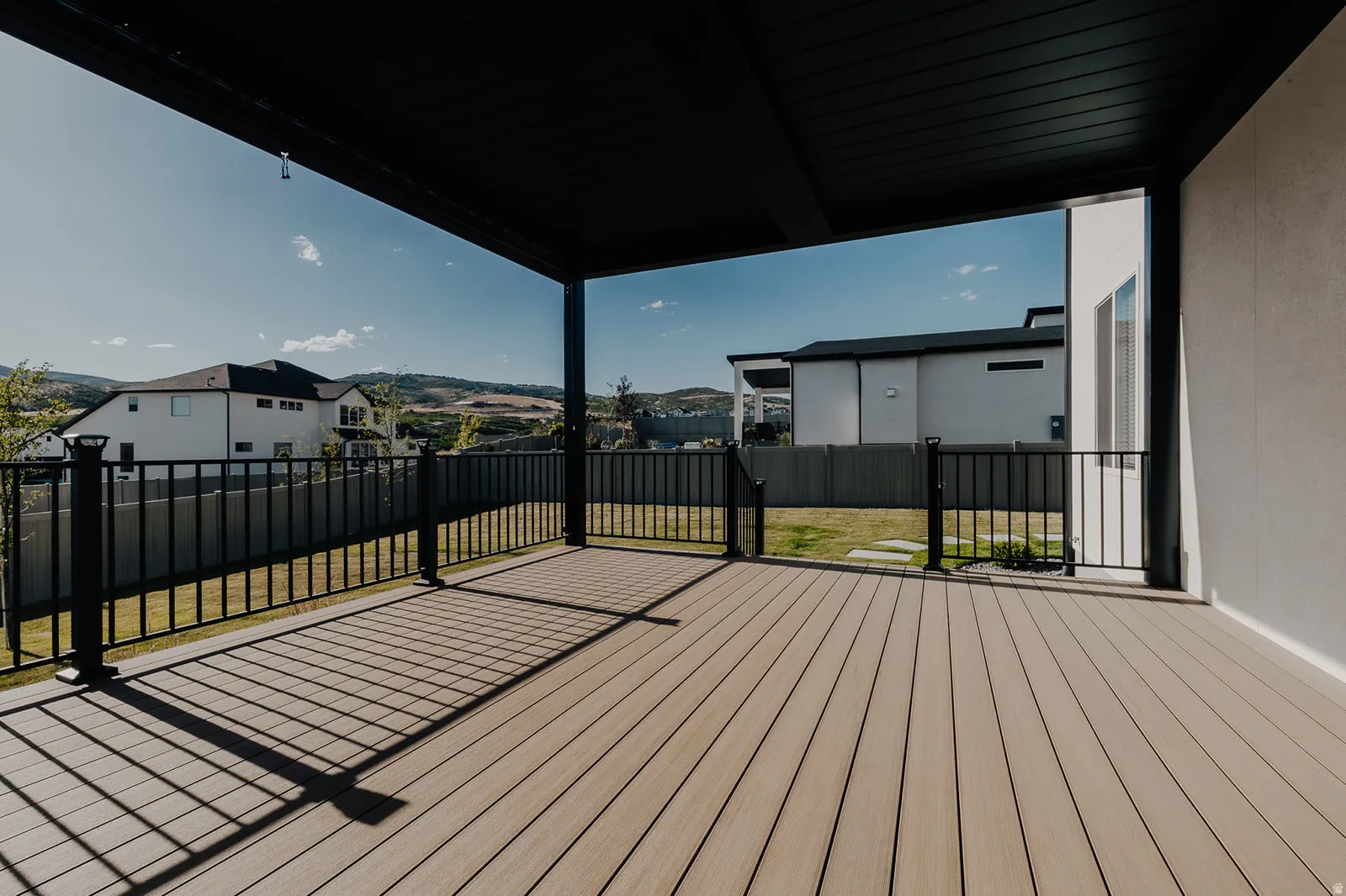 Covered outdoor deck with composite decking, black metal railings, and a stucco exterior wall