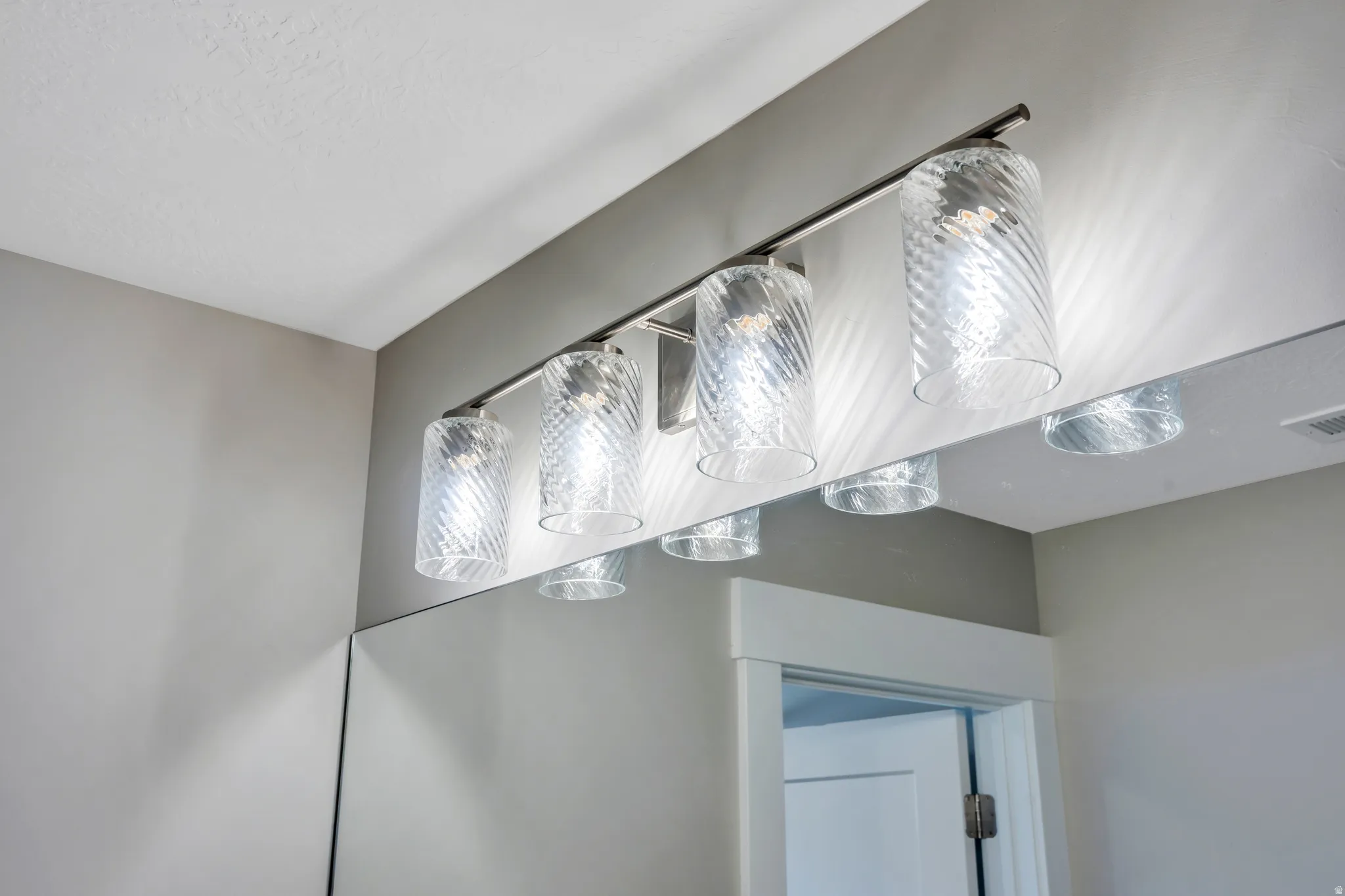 Four-light vanity fixture featuring clear, textured glass shades and a brushed metal base