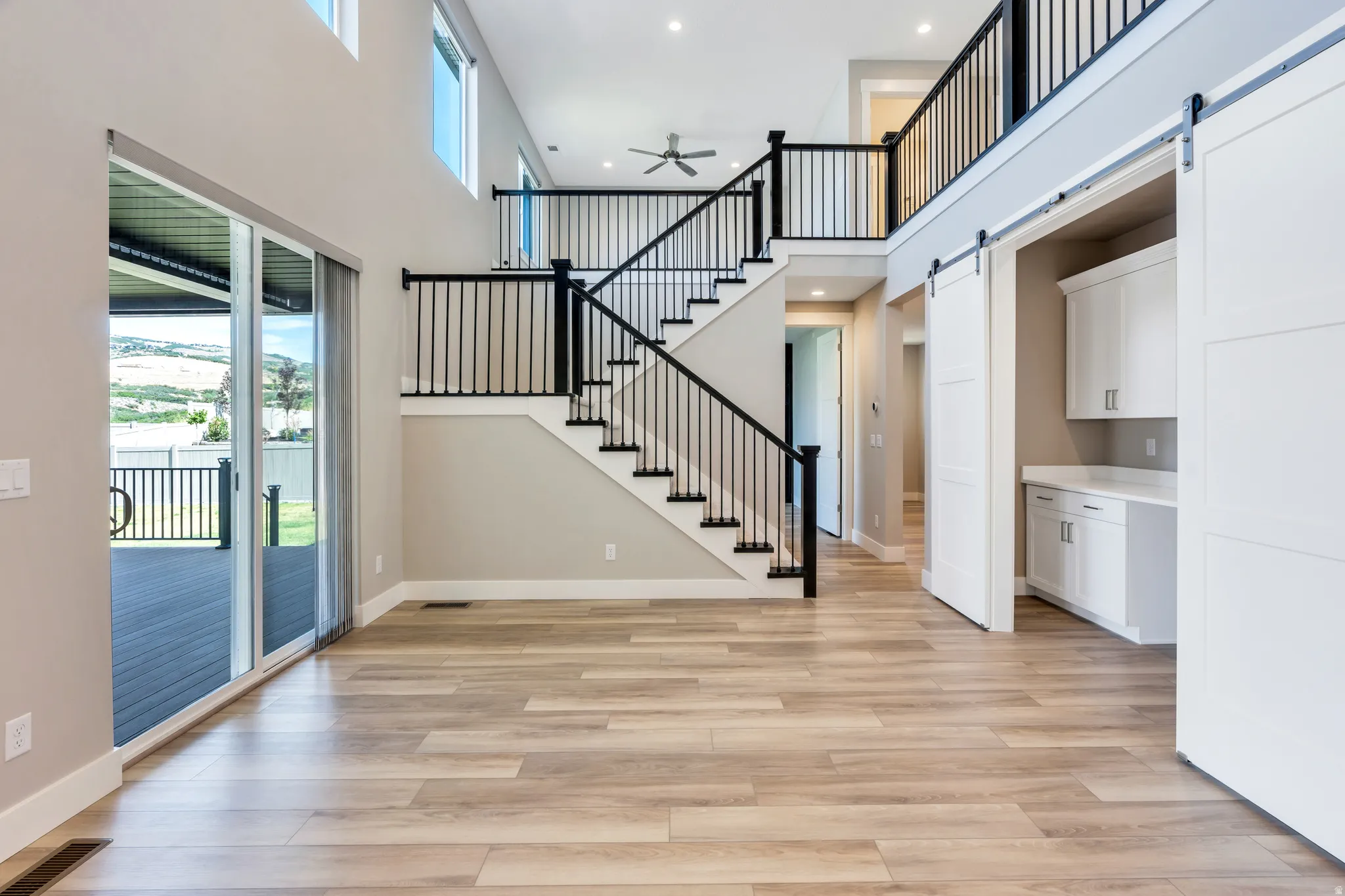 Two-story foyer featuring wood-finish flooring, a contemporary staircase with black railings, and a built-in desk area with white cabinetry and barn doors