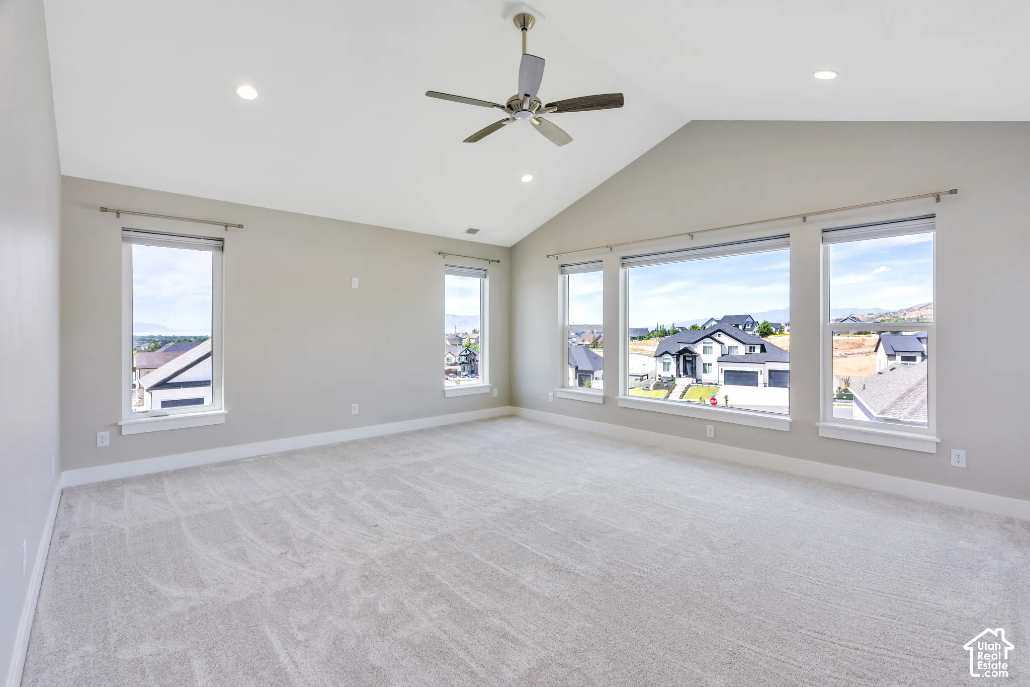 Spacious primary room featuring vaulted ceilings, recessed lighting, a ceiling fan, light-toned carpeting, and multiple windows providing ample natural light