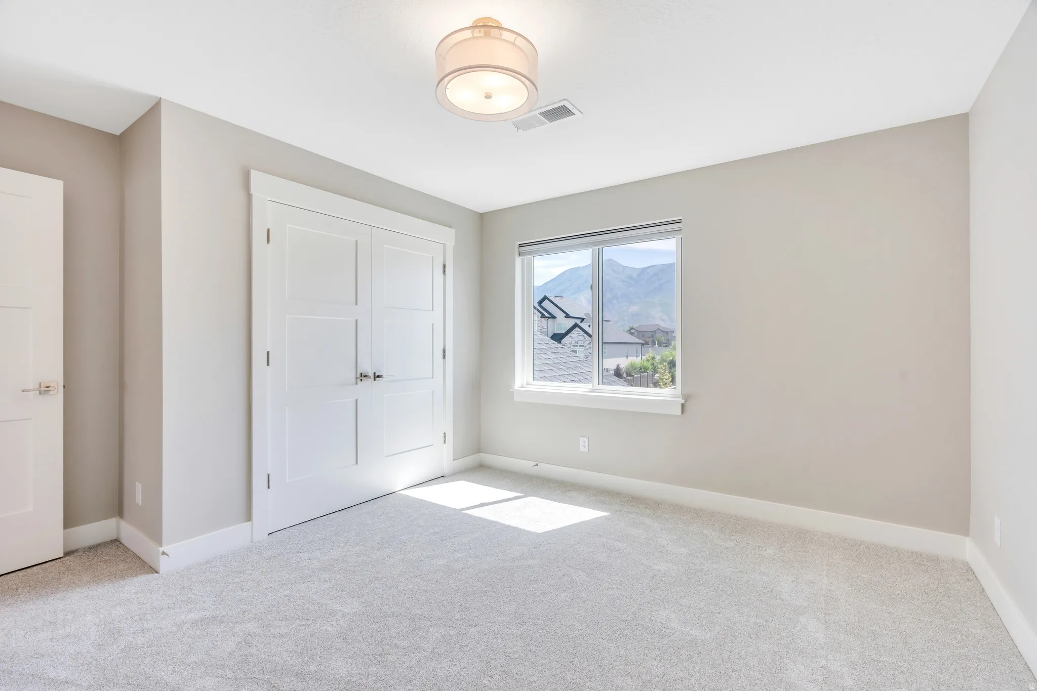 Neutral-toned room featuring a large window with mountain scenery, plush grey carpeting, white baseboards, and a contemporary ceiling light fixture