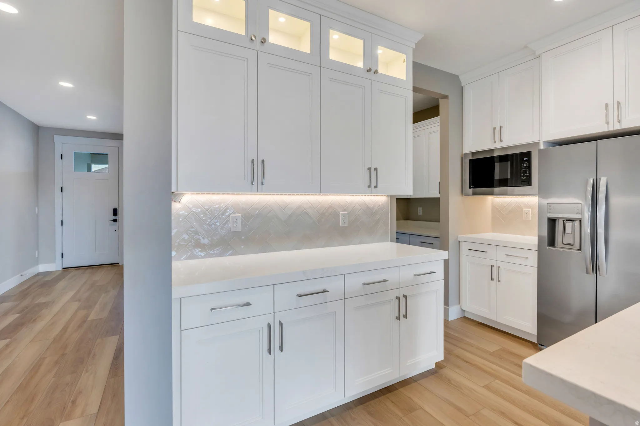 Contemporary kitchen featuring white shaker cabinetry, quartz countertops, a herringbone tile backsplash, and stainless steel appliances