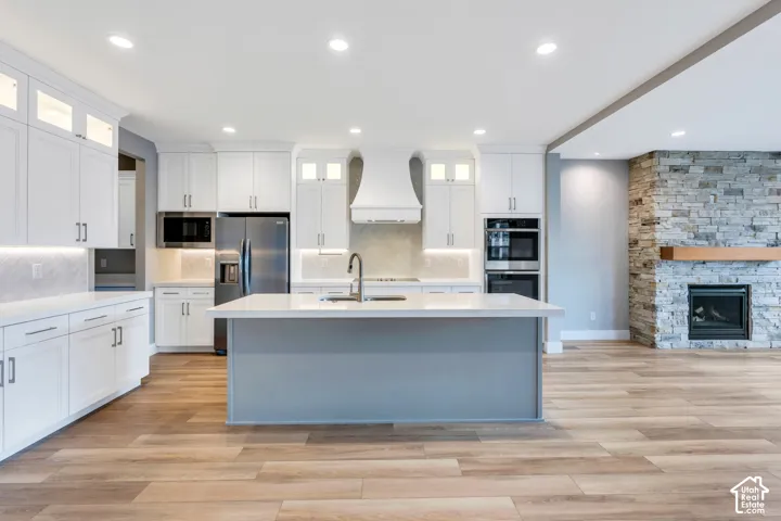 Open-concept kitchen featuring an island with a sink, white cabinetry with integrated lighting, stainless steel appliances, and wood-finish flooring