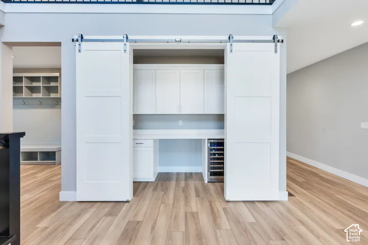 Built-in desk area featuring white cabinetry, a beverage refrigerator, and two white barn doors on a silver-tone track