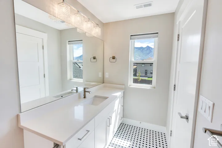 Bathroom featuring a full-width mirror, white vanity with integrated sink, and black and white penny tile flooring