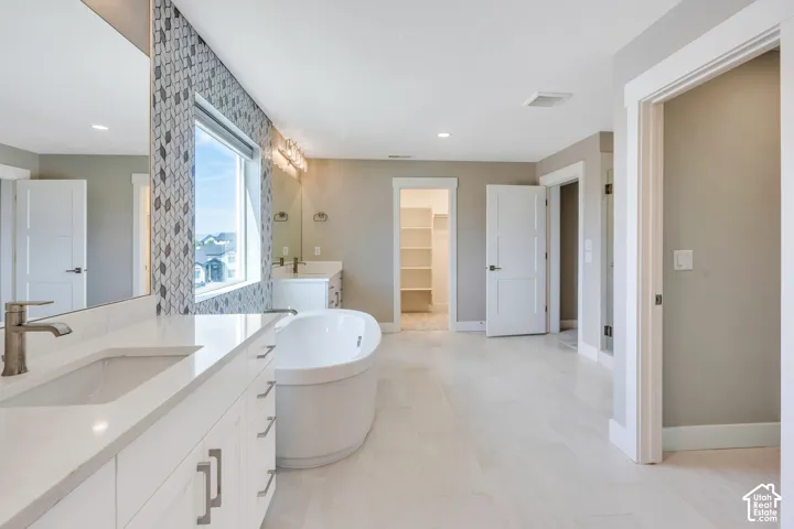 Primary bathroom with a spacious bathroom featuring a freestanding soaking tub, dual vanity with undermount sinks, patterned tile accent wall, and light-toned flooring
