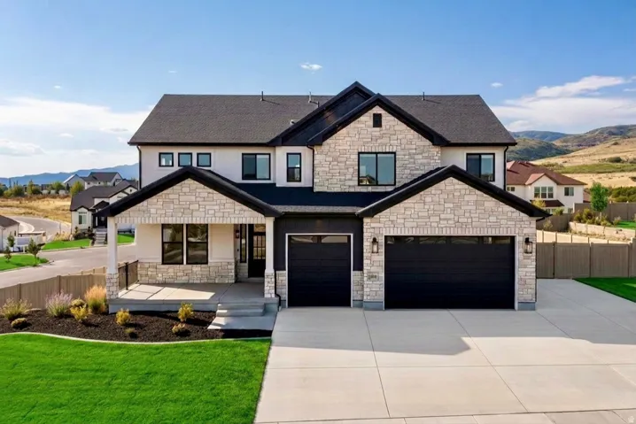 Contemporary two-story residence featuring a stone and stucco exterior, prominent black garage doors, a covered front porch, and a concrete driveway