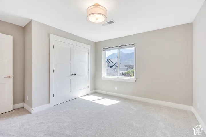 Neutral-toned room featuring a large window with mountain scenery, plush grey carpeting, white baseboards, and a contemporary ceiling light fixture