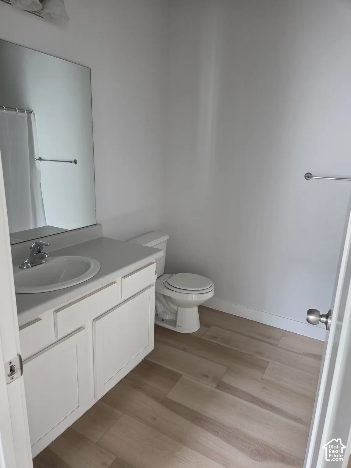 Bathroom featuring wood-finish flooring, a white vanity with an integrated sink, a large wall-mounted mirror, and a chrome towel bar