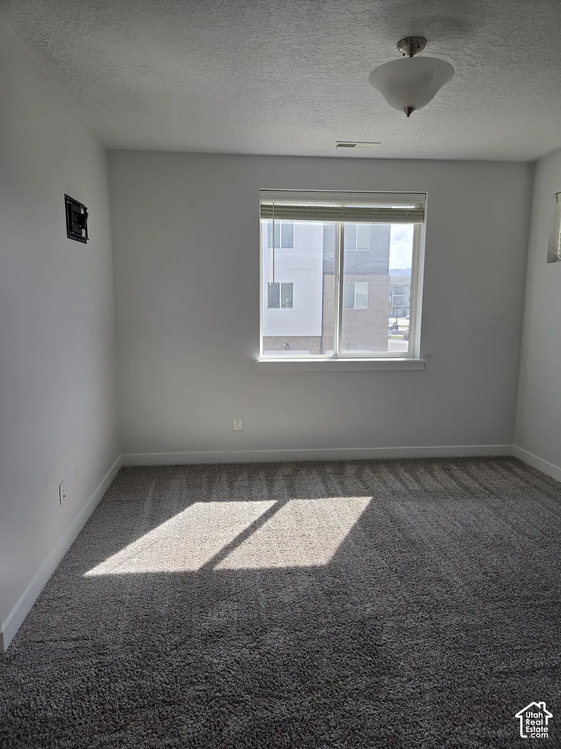 Spacious room featuring neutral carpeting, a large window with blinds, and a flush mount ceiling light fixture