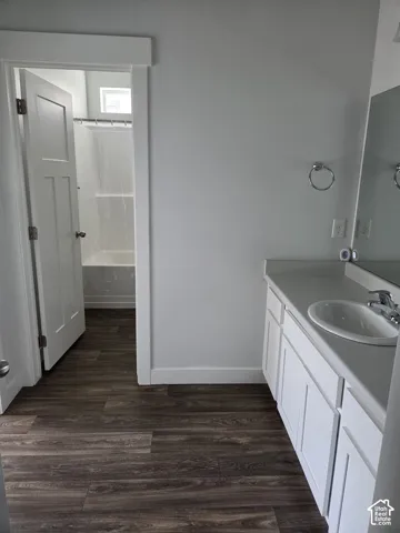 Full bathroom featuring a single vanity with an integrated sink, white cabinetry, and wood-finish flooring