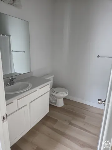 Bathroom featuring wood-finish flooring, a white vanity with an integrated sink, a large wall-mounted mirror, and a chrome towel bar