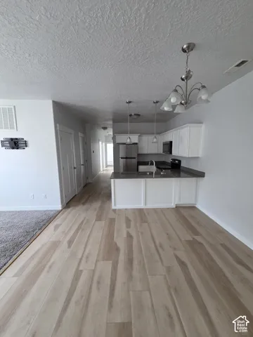 Open-concept kitchen featuring white cabinetry, stainless steel appliances, dark countertops, and light wood-finish flooring
