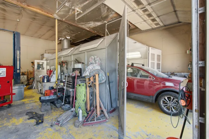 Spacious commercial garage featuring a vehicle lift, concrete flooring, and an integrated paint booth