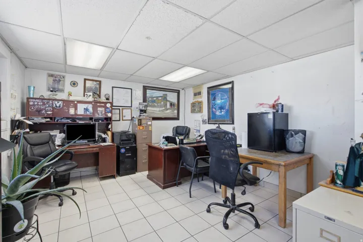 Commercial office space featuring white tile flooring, white walls, and a dropped ceiling with integrated lighting panels