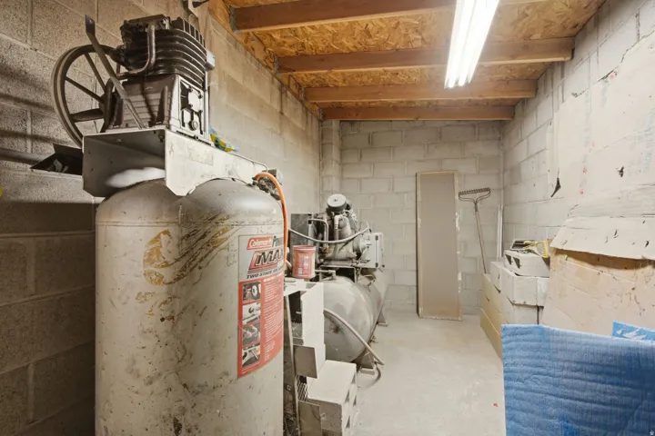 Utility room featuring exposed wooden ceiling joists, concrete block walls, and fluorescent lighting