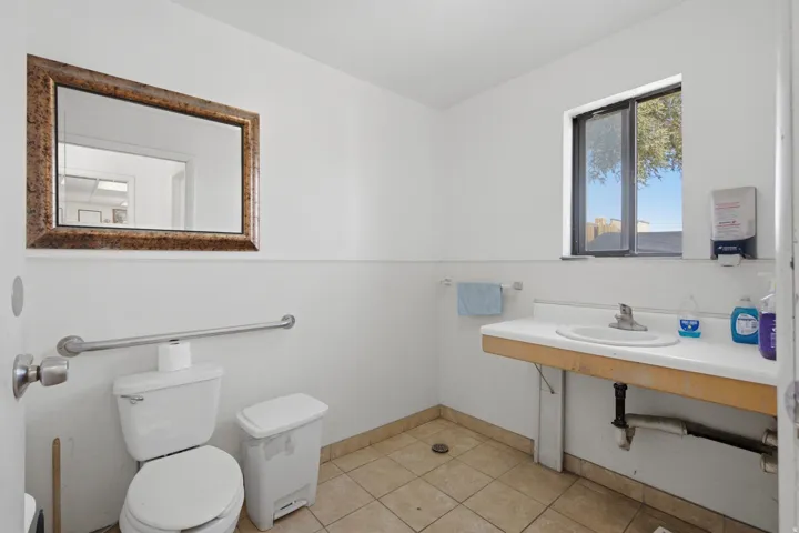 White-painted interior featuring a rectangular vanity with an integrated sink, a window providing natural light, and tiled flooring