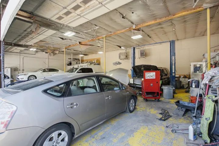 Commercial garage space featuring two vehicle lifts, overhead lighting fixtures, and a roll-up garage door
