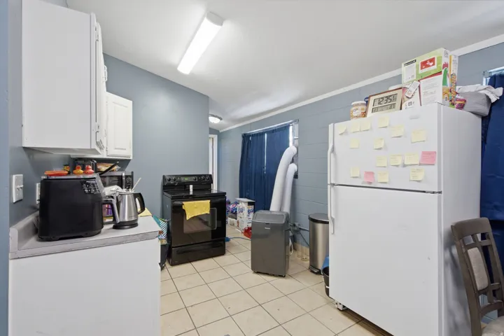 Kitchen featuring white upper cabinetry, a black electric range, and light-toned tile flooring