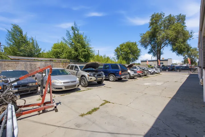 Paved lot with ample parking capacity, bordered by a concrete block wall and mature trees