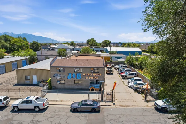 Two-story commercial building featuring a fenced lot, asphalt parking area, and an adjacent metal-sided building with garage doors