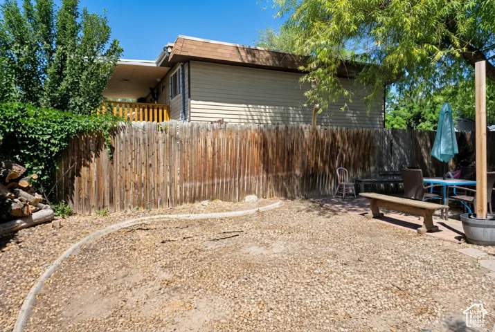 Expansive gravel yard featuring a wood privacy fence, mature trees, and a raised wooden deck with railings