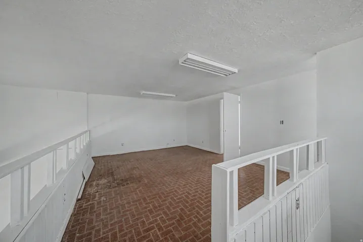 Spacious room featuring brick-patterned flooring, bright white walls, and overhead fluorescent lighting
