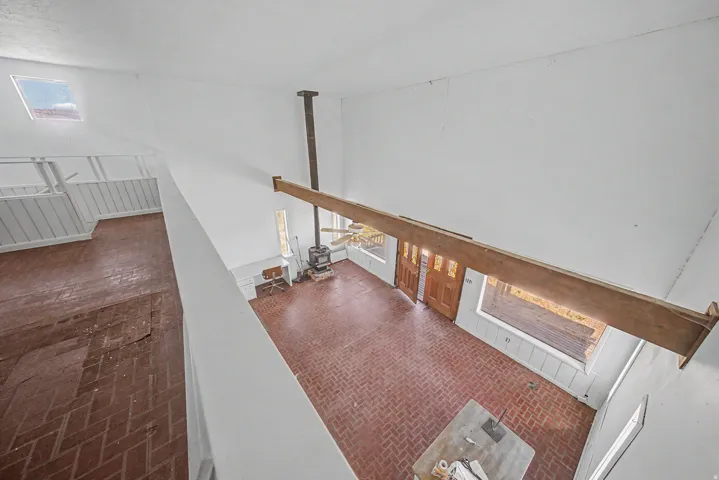 Vaulted ceiling great room featuring brick flooring, a wood-burning stove with an exposed flue, and a wood support beam