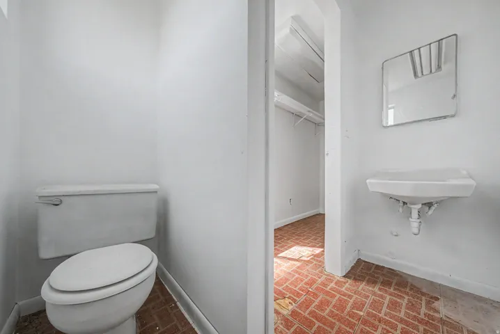 Powder room with a wall-mounted sink, rectangular mirror, and brick-patterned tile flooring